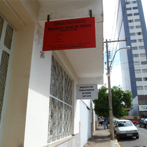 A placa vermelha do escritório de Alfenas/MG se destaca diante do prédio de paredes brancas. 