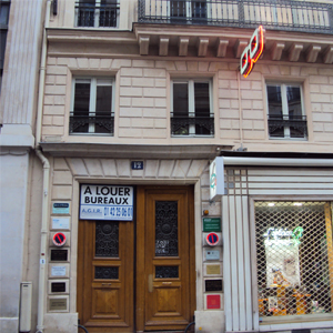As placas ao lado da porta de madeira maciça indicam inúmeras salas ocupadas no prédio parisiense. Do lado direito, a sexta placa corresponde a uma banca advocatícia, da cidade luz, Paris.